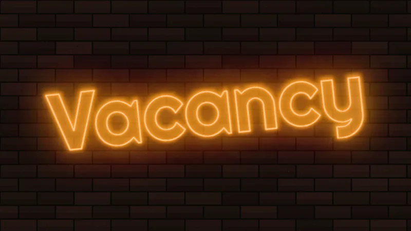 Orange neon outline sign reading Vacancy, tilted on a brick wall like a motel sign